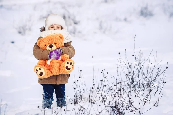 Bonne petite fille tient dans ses bras un ours en peluche orange en hiver à l'extérieur . — Photo