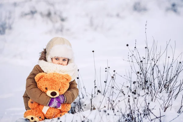 Joyeux petit caucasien fille assis sur la neige et tenant un ours en peluche orange — Photo