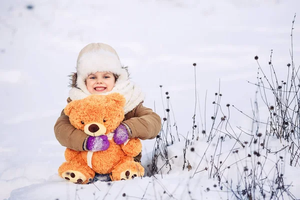 Joyeux petit caucasien fille assis sur la neige et tenant un ours en peluche orange — Photo