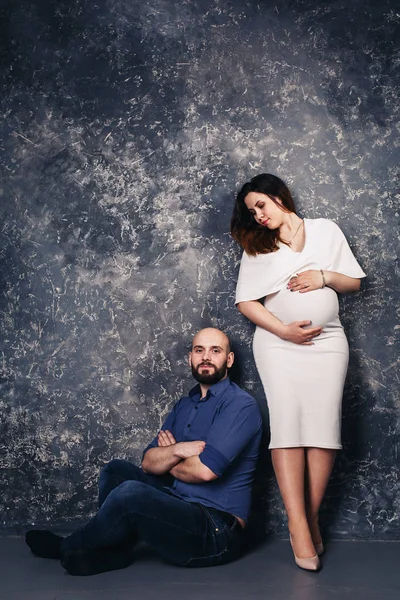 Das glückliche junge schwangere Paar im Studio vor dunklem Hintergrund. Familienbeziehungskonzept. — Stockfoto