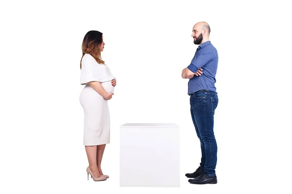 Eine schwangere Frau und ein bärtiger Mann schauen sich ernsthaft an, und dazwischen steht ein leerer weißer Sockel — Stockfoto