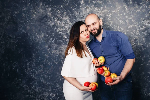 Heureuse jeune famille végétalienne. une fille enceinte et un homme barbu tenant des pommes dans leurs mains et faisant des grimaces drôles — Photo