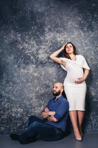 Das glückliche junge schwangere Paar im Studio vor dunklem Hintergrund. Familienbeziehungskonzept. — Stockfoto