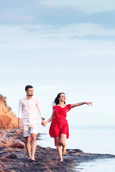 Garçon et fille longent le bord de la mer en se tenant la main. Femme montre doigt à la mer . — Photo