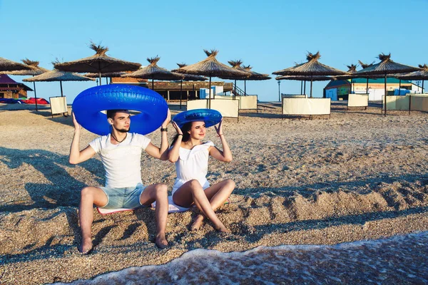 Mężczyzna i kobieta siedzą na plaży i trzymając nadmuchiwane koła. koncepcja lato morze wakacje. — Zdjęcie stockowe