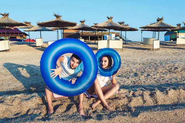 Mężczyzna i kobieta siedzą na plaży i trzymając nadmuchiwane koła. koncepcja lato morze wakacje. — Zdjęcie stockowe