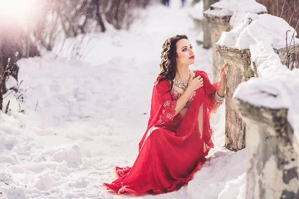 Beautiful young girl dancing belly dance in red dress in winter in a park on the snow. — Stock Photo, Image