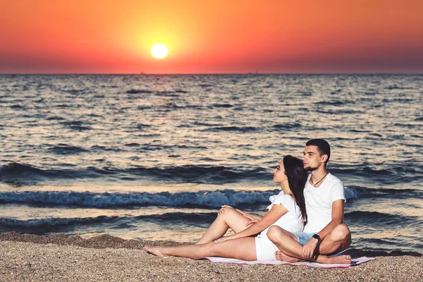 Un jeune couple amoureux se repose et profite du lever du soleil au bord de la mer . — Photo