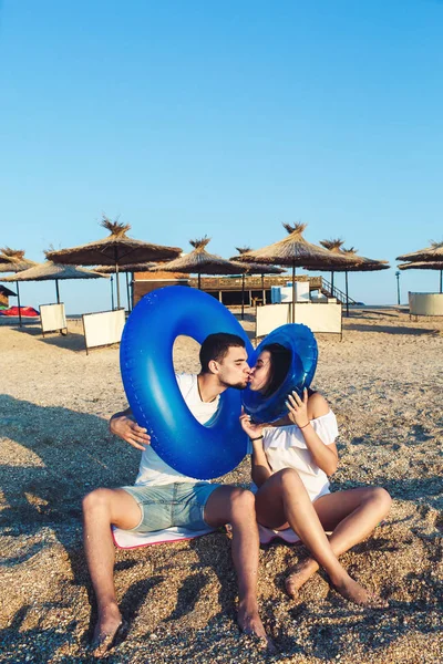 Hombre y mujer están sentados en la playa y sosteniendo círculos inflables. concepto de vacaciones de verano mar . — Foto de Stock