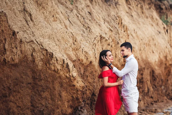 Hermosa mujer y barbudo hombre abrazo cerca de arcilla roca . — Foto de Stock