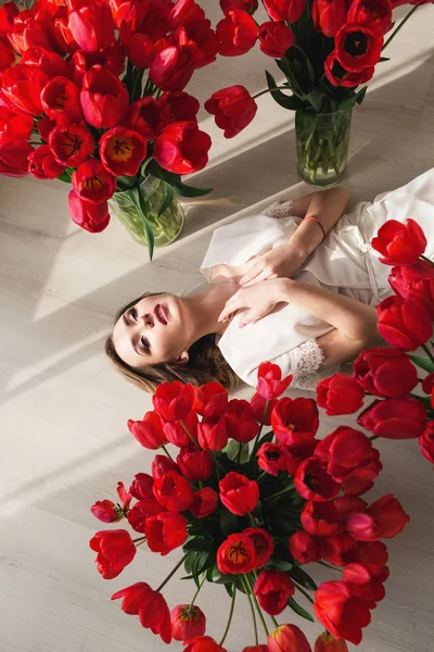 Krásná mladá dívka v peignoir leží na podlaze mezi velké Kytice tulipánů. 8. března koncept. — Stock fotografie