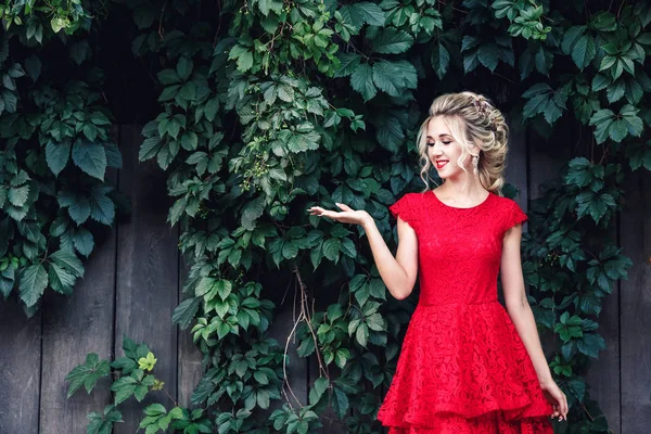 Atractiva joven rubia en vestido rojo sostiene espacio de copia en la palma contra el telón de fondo de viñedo salvaje . — Foto de Stock