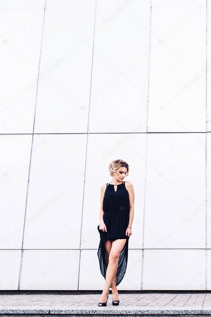 elegant young girl in black dress posing against a gray wall.