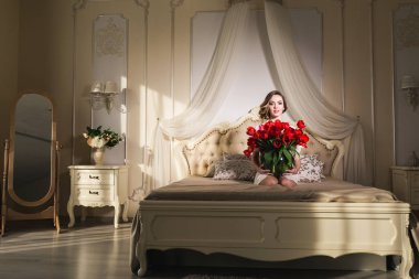 Güzel bir genç kız yatakta oturan ve bir sürü kırmızı lale vazo içinde tutarak. Mart 8 kavram.