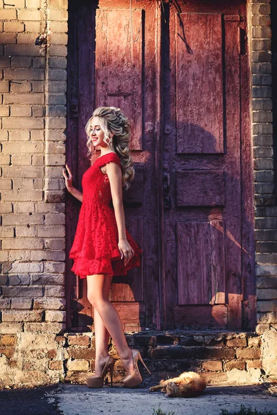 Aantrekkelijke jonge blonde in rode jurk poseren op de achtergrond van een oude bakstenen gebouw. — Stockfoto