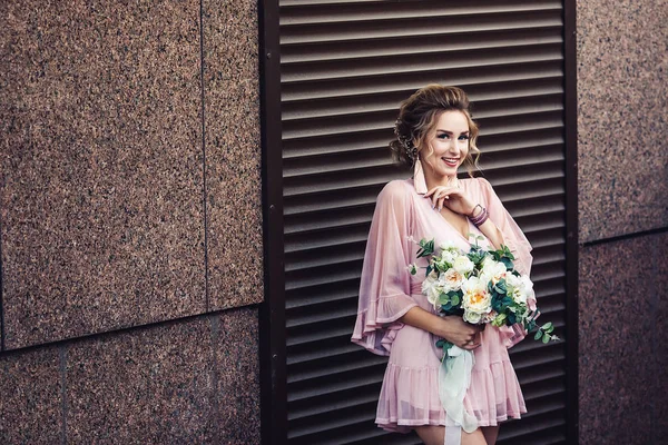 Jovem atraente em um vestido curto com um buquê de flores posando perto da parede de granito com persianas . — Fotografia de Stock