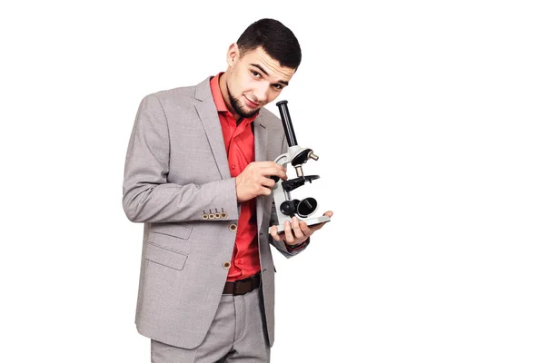 Joven barbudo con estilo en un traje gris y un microscopio en sus manos —  Fotos de Stock
