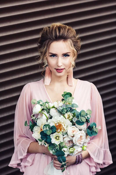 Atractiva joven en un vestido corto con un ramo de flores posando cerca de la pared de granito con persianas enrollables . — Foto de Stock