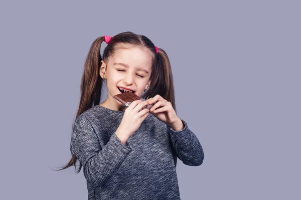 Little joyful girl eats chocolate and shows her teeth affected by caries. — Stock Photo, Image