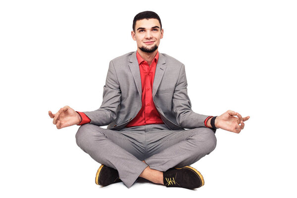 stylish young bearded guy in a gray suit meditates sitting in the lotus position