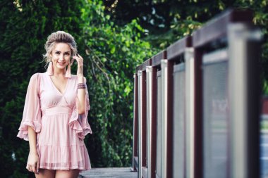 yeşil yeşillik zemin üzerine çelik çit yakınındaki poz kısa pembe elbiseli çekici genç kız.