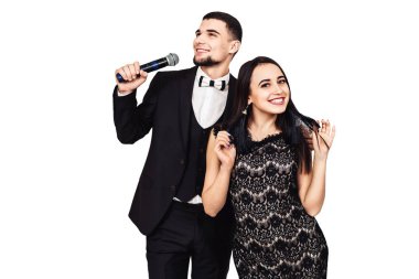 siyah bir takım elbise içinde sakallı adam elinde bir mikrofon ve bir siyah gece elbisesi içinde güzel bir kız ile