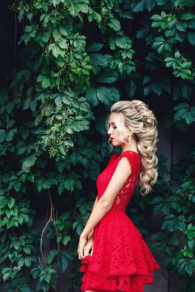 Attraktive junge blonde Mädchen in rotem Kleid posiert in der Nähe eines wilden Weinbergs. — Stockfoto