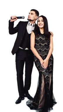 siyah bir takım elbise içinde sakallı adam elinde bir mikrofon ve bir siyah gece elbisesi içinde güzel bir kız ile
