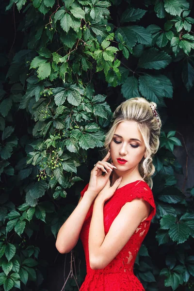 Atractiva joven rubia en vestido rojo posando cerca de un viñedo salvaje . — Foto de Stock