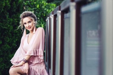 yeşil yeşillik zemin üzerine çelik çit yakınındaki poz kısa pembe elbiseli çekici genç kız