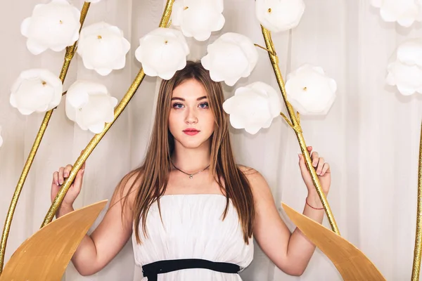 Hermosa chica de pelo largo posando entre grandes flores artificiales — Foto de Stock