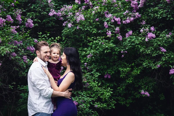 Alegre familia feliz abrazo cerca de arbustos de flores lila — Foto de Stock
