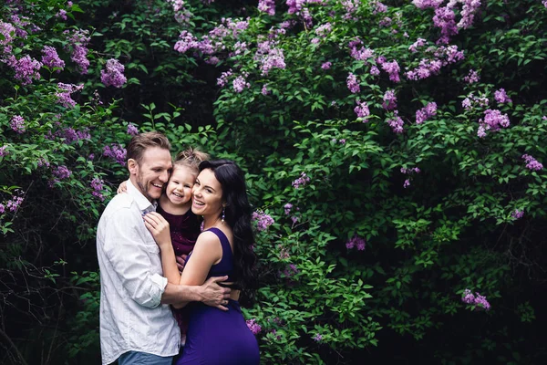 Alegre família feliz abraçando perto de arbustos floridos lilás — Fotografia de Stock
