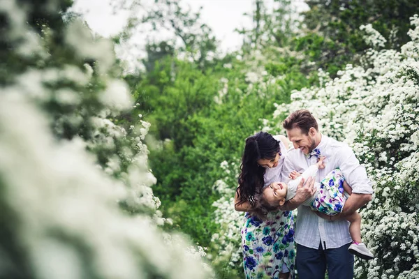 Pai alegre e mãe estão se divertindo brincando com sua filhinha. família descansando na natureza entre arbustos spirea — Fotografia de Stock