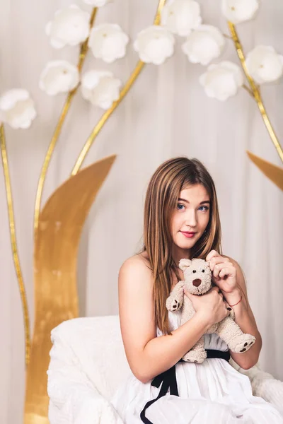 Hermosa chica de pelo largo con un osito de peluche en sus manos sobre un fondo floral — Foto de Stock