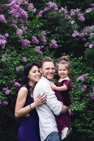 Весела щаслива сім'я обіймається біля бузкових квітучих кущів — стокове фото