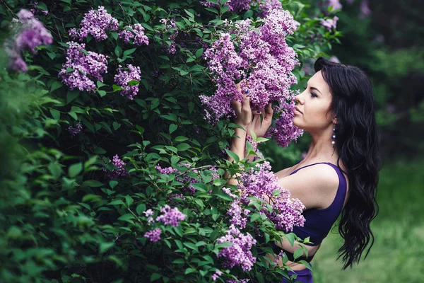 attractive woman in purple dress posing near lilac flowering bushes