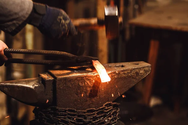 The blacksmith manually forging the red-hot metal on the anvil in smithy with spark fireworks. — Stock Photo, Image