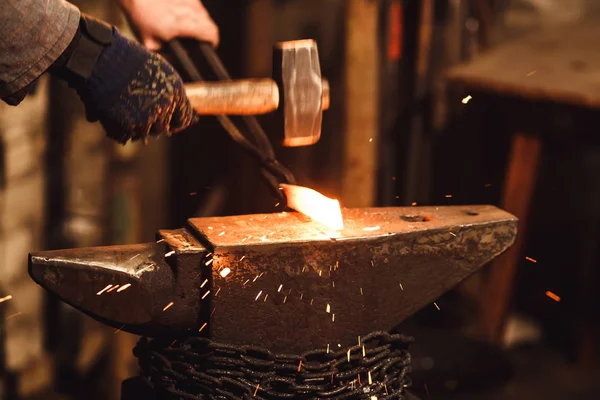 El herrero forja manualmente el metal al rojo vivo en el yunque en la herrería con fuegos artificiales de chispa . — Foto de Stock