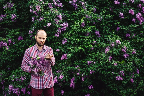 man calls to himself. young bearded man with a bouquet of flowers near lilac blossoms.
