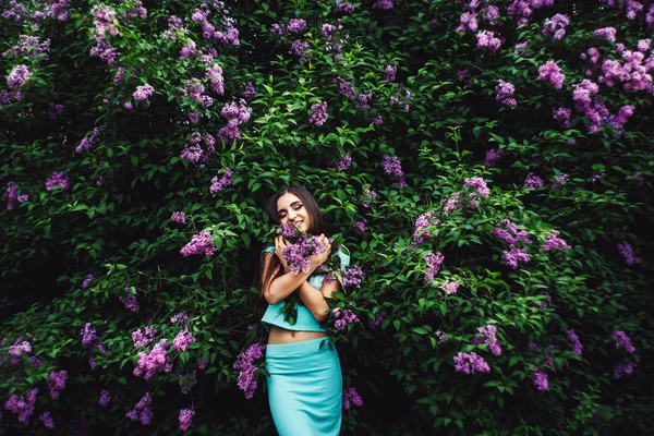 Nádherné jarní. Roztomilá mladá dívka se těší přírody mezi kvetoucí šeřík a drží kytici. — Stock fotografie