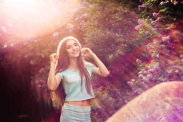 Maravilhosa primavera. Uma bela jovem goza de natureza e luz solar entre o lilás florescente . — Fotografia de Stock