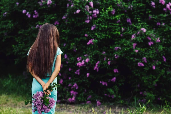 Maravillosa primavera. Linda chica joven disfruta de la naturaleza entre la flor de lila y sostiene un ramo . — Foto de Stock
