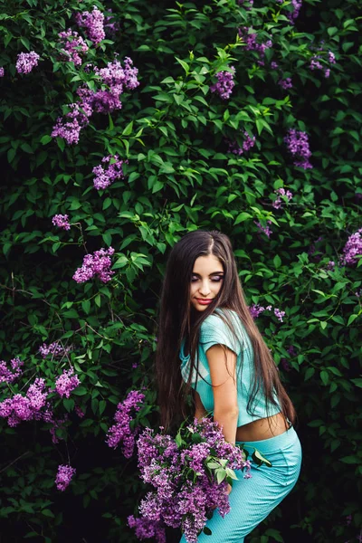 Prachtige lente. Schattig jong meisje geniet van de natuur onder de bloeiende lila en houdt een boeket. — Stockfoto