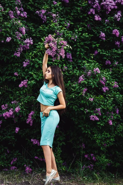 Nádherné jarní. Roztomilá mladá dívka se těší přírody mezi kvetoucí šeřík a drží kytici. — Stock fotografie