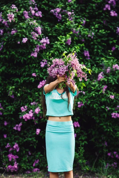 Prachtige lente. Schattig jong meisje geniet van de natuur onder de bloeiende lila en houdt een boeket. — Stockfoto