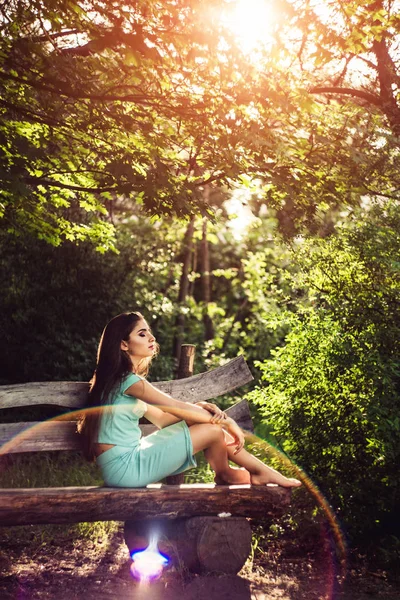 Prachtige lente. Mooi jong meisje geniet van natuur en zonlicht zittend op een houten bankje in het park. — Stockfoto