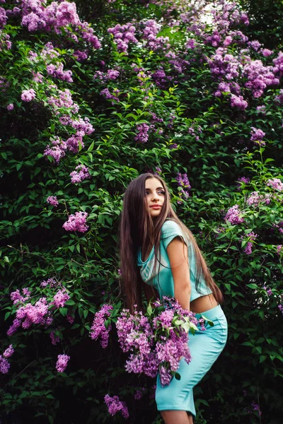 Maravillosa primavera. Linda chica joven disfruta de la naturaleza entre la flor de lila y sostiene un ramo . — Foto de Stock