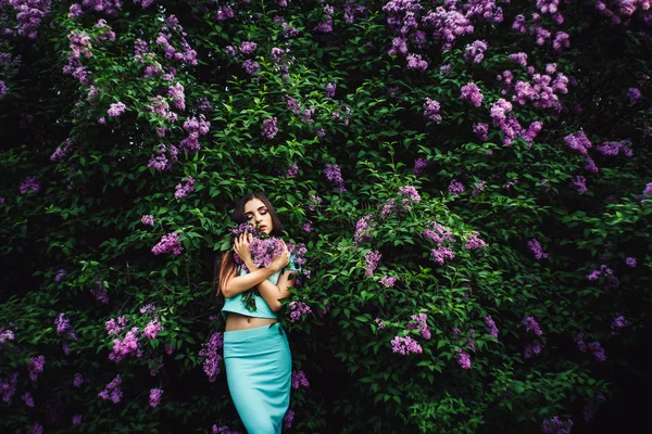 Prachtige lente. Schattig jong meisje geniet van de natuur onder de bloeiende lila en houdt een boeket. — Stockfoto