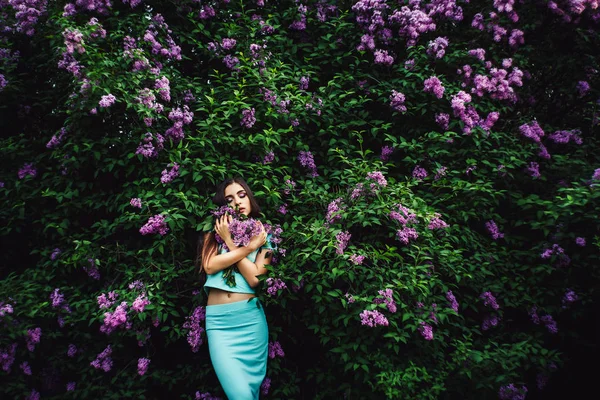 Nádherné jarní. Roztomilá mladá dívka se těší přírody mezi kvetoucí šeřík a drží kytici. — Stock fotografie